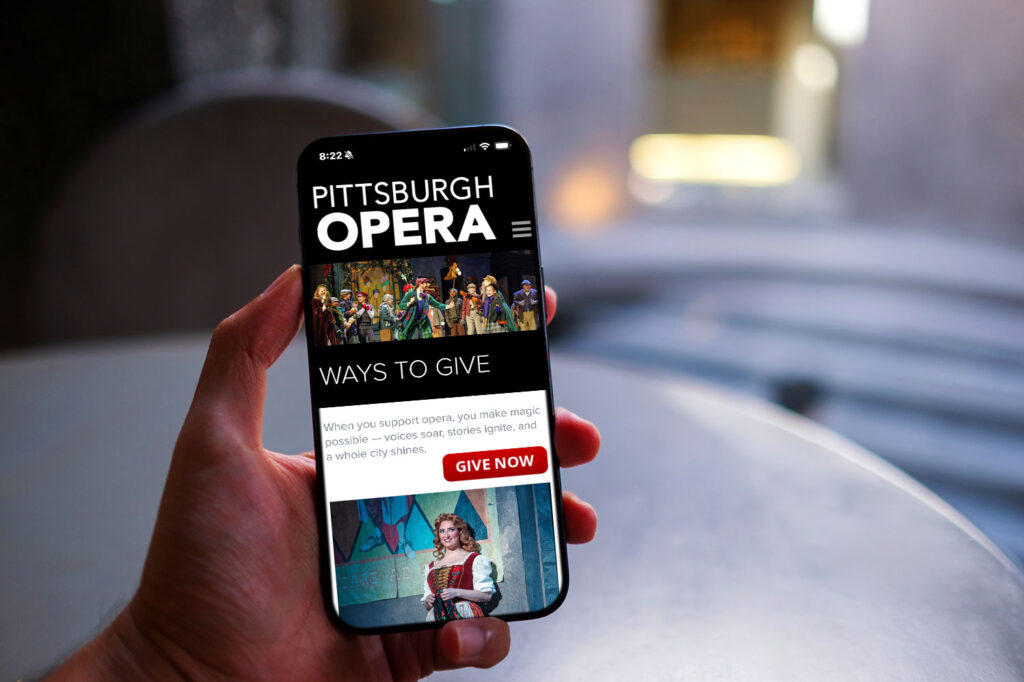 Person holding smartphone displaying Pittsburgh Opera website